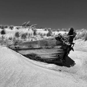 A vintage boat rests on the sandy shore in a black and white photograph