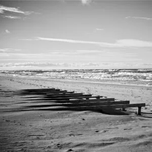 A black and white photo depicting a peaceful beach with wooden benches